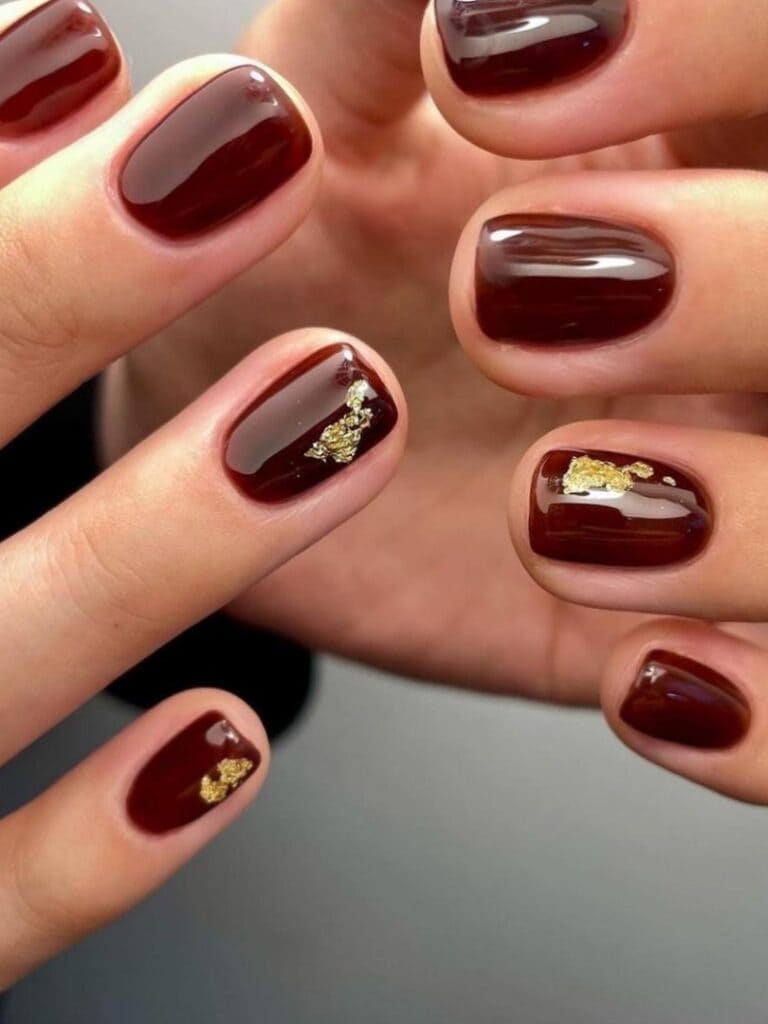 Short burgundy nails with a gold foil accent