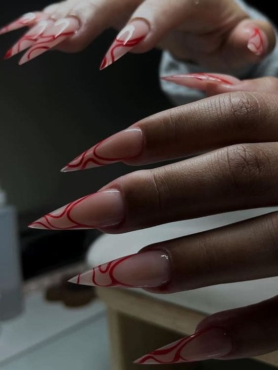 long stiletto nude nails with red swirls 